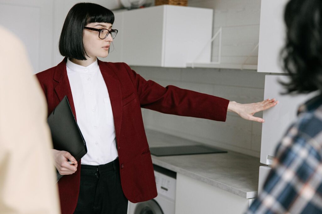 A female real estate agent demonstrates a modern kitchen to potential buyers in an apartment.